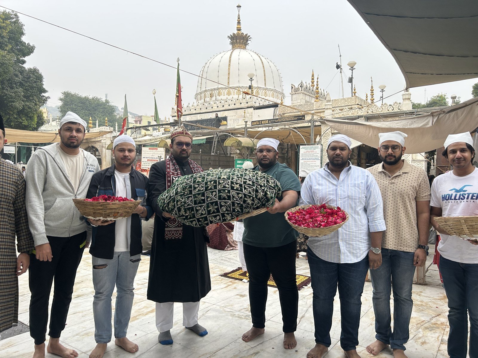 A group holding a patterned cloth and trays of flowers in the Dargah courtyard