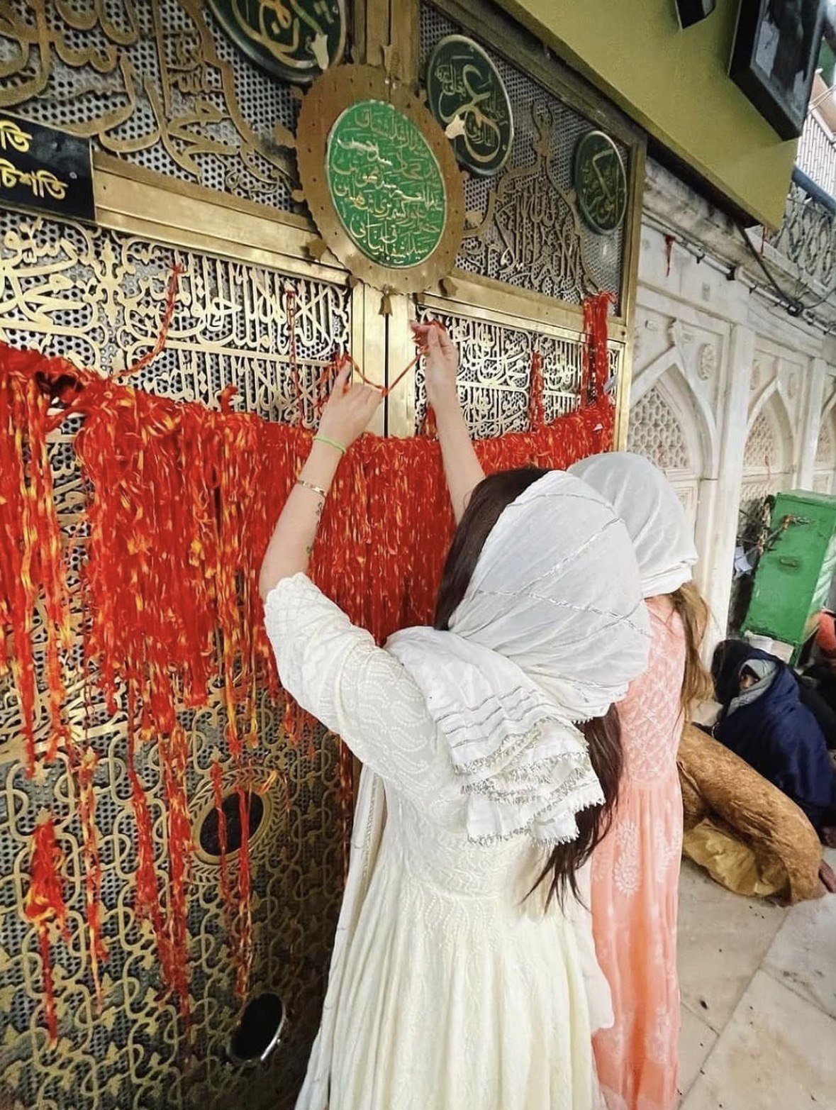A visitor reaching toward a red and gold decorated lattice
