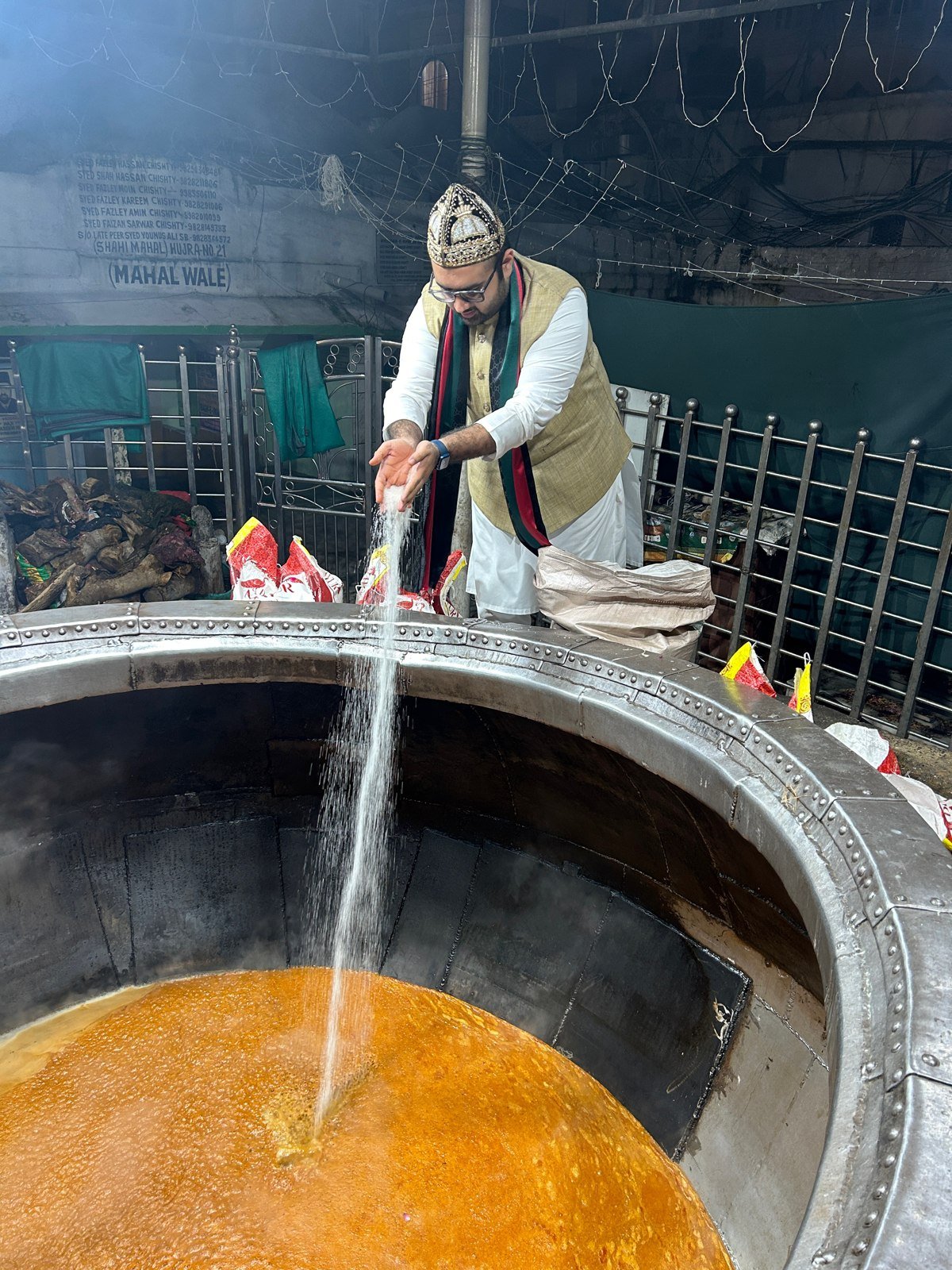 A man pours white ingredients from his hands into an orange mixture in a large cauldron