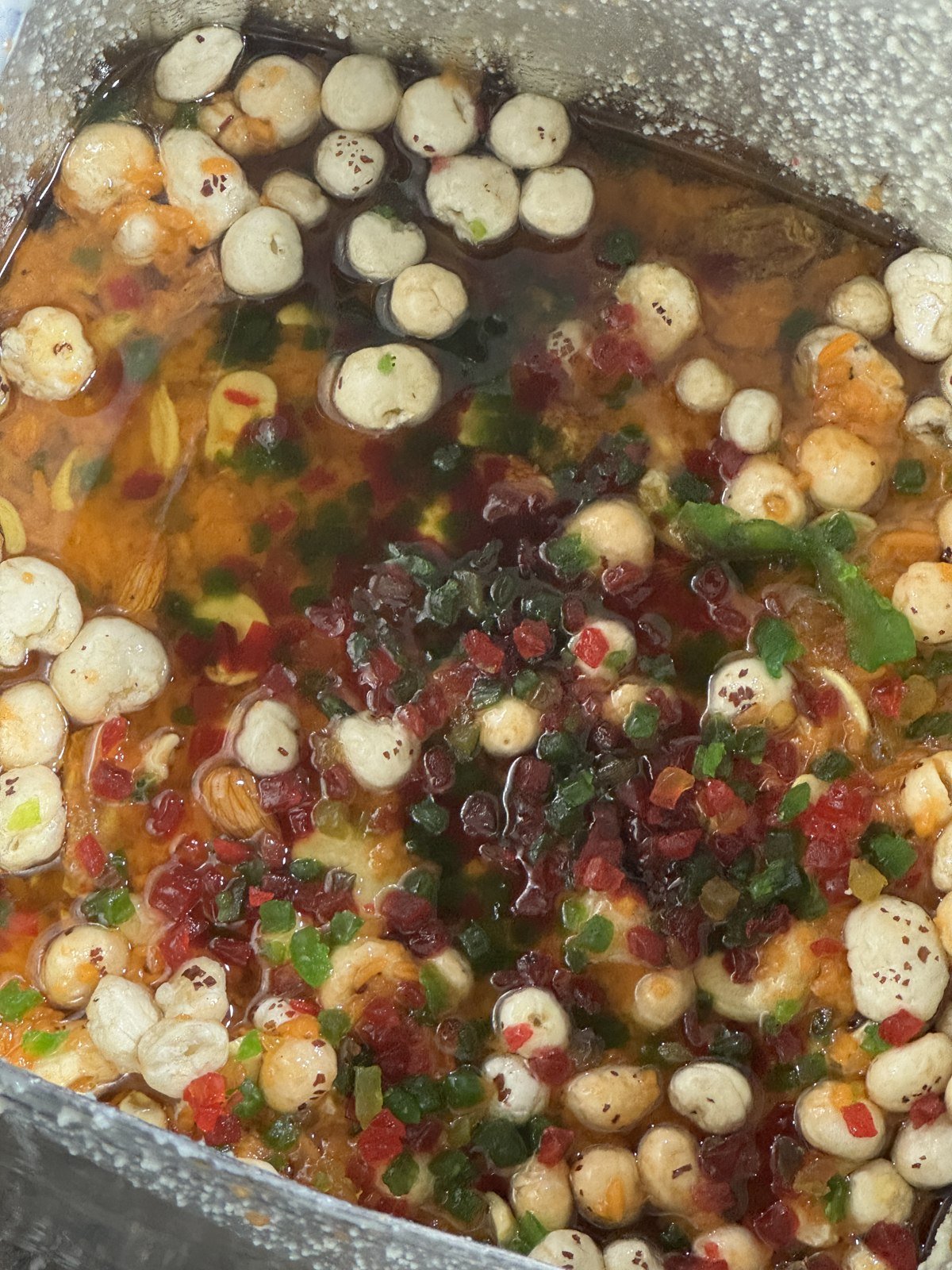 Round white pieces and red and green ingredients in liquid inside a cooking vessel