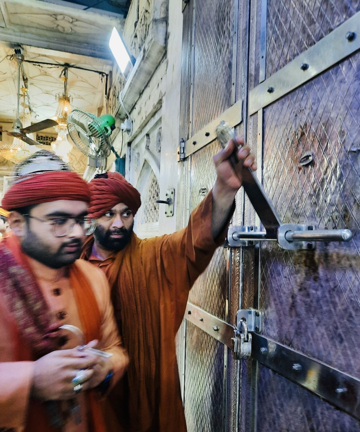 Attendant handling the metal fitting on a doorway at Ajmer Sharif